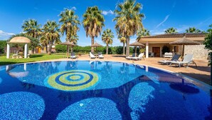 A swimming pool with a circular mosaic design, surrounded by palm trees and lounge chairs.