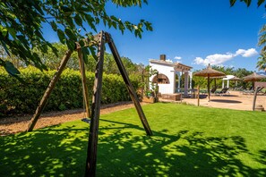 A well-maintained garden with a wooden swing set, a white gazebo, and a pool area with lounge chairs.