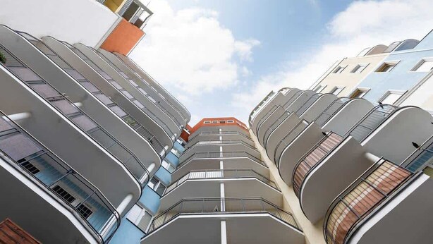 A multi-story building with balconies, a clear sky, and a visible orange building in the background. - Cozy Studio close to the Beach | Sauna and Gym (Kolobrzeg)
