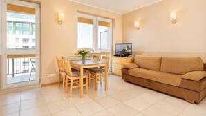A modern living room with a sofa, a dining table with chairs, and a TV. - Cozy Studio close to the Beach | Sauna and Gym (Kolobrzeg)
