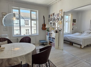 A room with a dining table, chairs, a bookshelf, a guitar, and a bed. - City Apartment in Copenhagen with 1 bedrooms sleeps 4 (Copenhagen)
