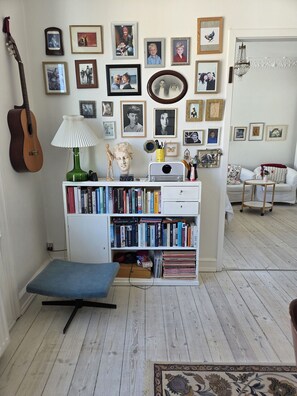 A room with a bookshelf, a guitar, a lamp, a bust, and a chandelier.