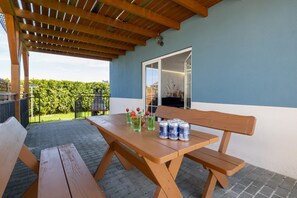 Un patio al aire libre con una mesa y bancos de madera, una pérgola arriba y vistas a un paisaje verde.