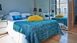 A modern bedroom with a large mirror, a bed with blue and yellow bedding, and a nightstand with a lamp.