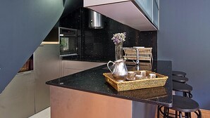 A modern kitchen with a black countertop, stainless steel appliances, and a small dining area with wicker chairs and stools.