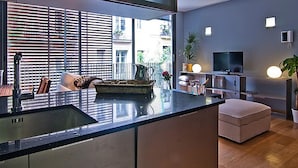 A modern kitchen with a large island, a dining area with a TV, and a balcony with a view of buildings.