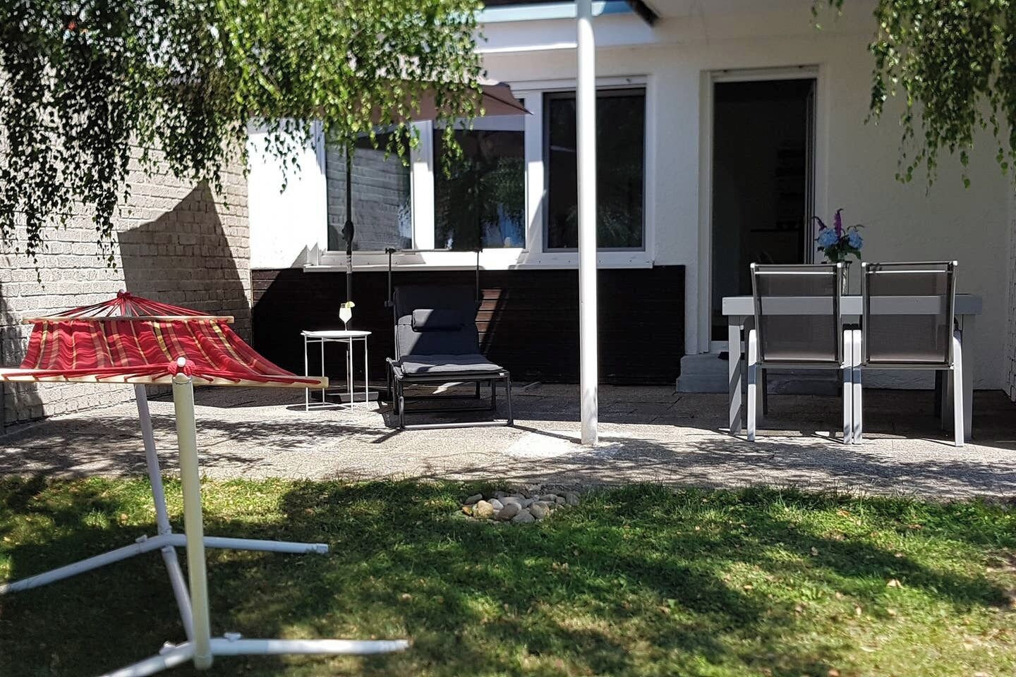 A patio area with a red umbrella, two lounge chairs, and a small table with a glass.