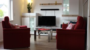 A modern living room with two red sofas, a glass coffee table, a flat-screen TV, and a wooden cabinet with glass doors. - High quality, modern with infrared sauna. Awarded 4 stars by the DTV. (Lierschied)