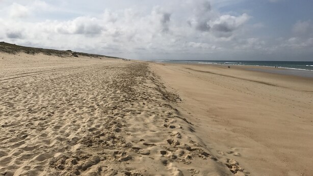 Ein weiter Sandstrand mit Fußabdrücken und freier Sicht auf das Meer.
