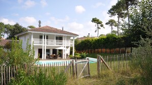 Ein zweigeschossiges Haus mit Balkon, Schwimmbad und Holzzaun.