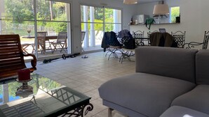 Ein großzügiger Wohnbereich mit einem großen Glasfenster, das auf eine Terrasse führt, einem grauen Sofa und einem Glastisch.
