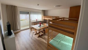 Ein Zimmer mit Etagenbetten, einem Esstisch, Stühlen, einem kleinen Schreibtisch und einer Heizung.