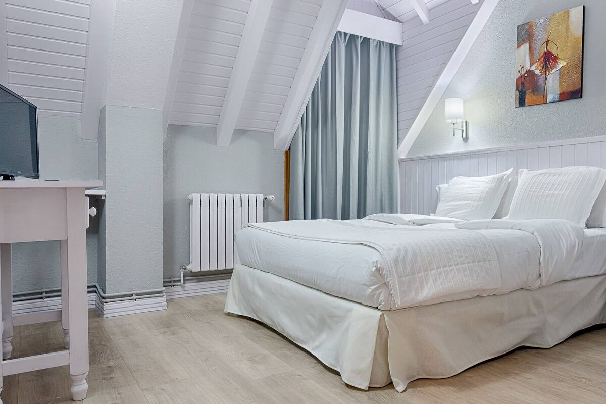 A bedroom with a bed, a desk, a radiator, and a painting on the wall.