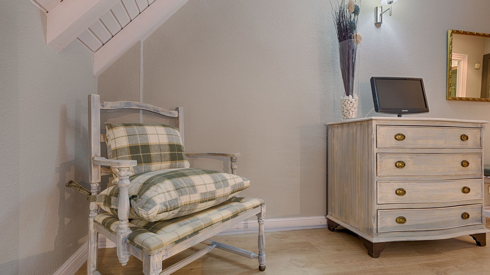 A room with a plaid-patterned chair, a wooden dresser with brass handles, and a television on top.