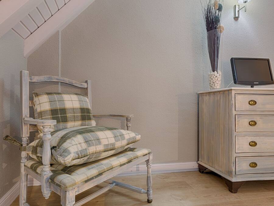 Una habitación con una silla de estampado escocés, un aparador de madera con tiradores de latón y un televisor encima.