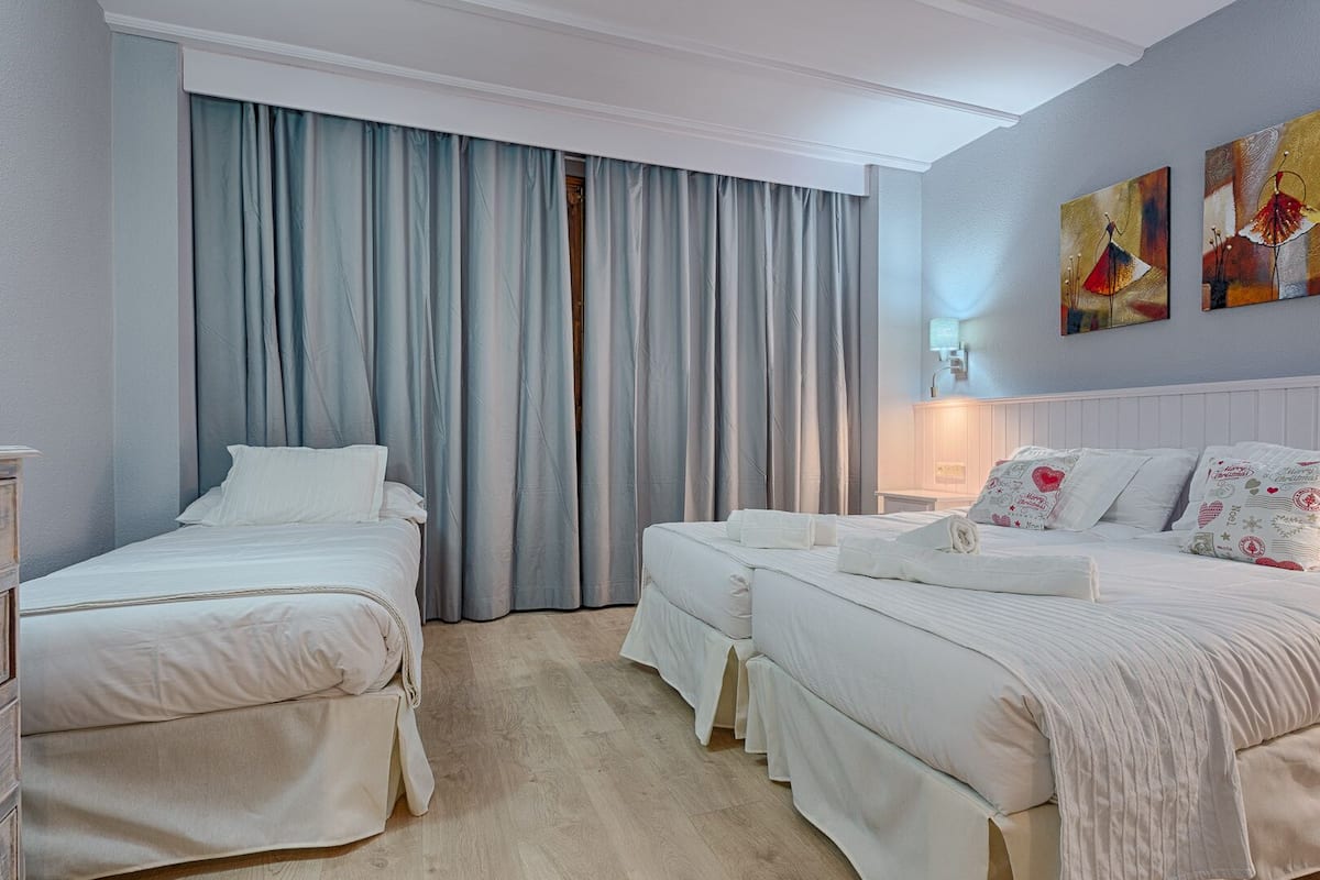 A hotel room with two single beds, a double bed, and a nightstand with a lamp.