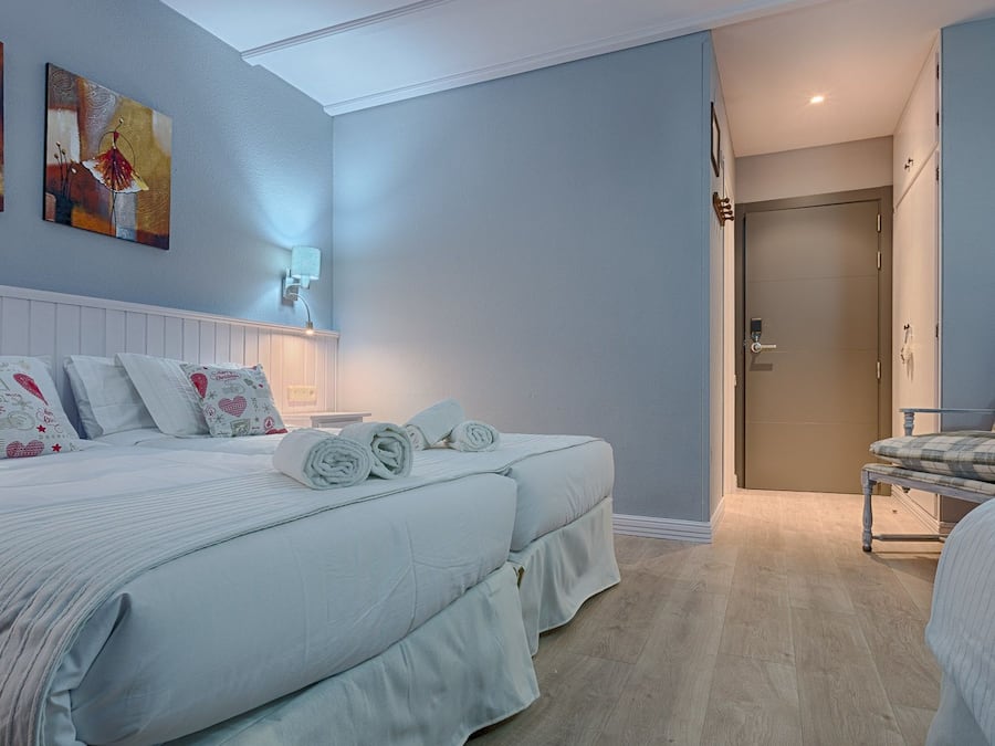 A bedroom with two beds, a nightstand, a dresser, and a door leading to another room.