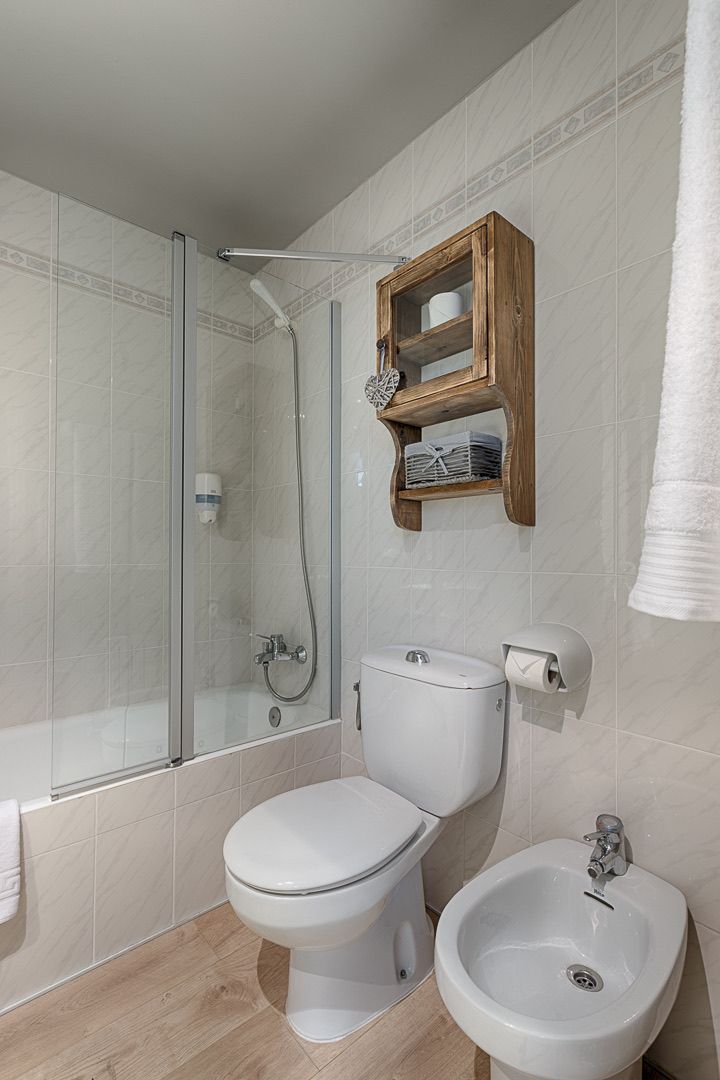 Un baño moderno con ducha envuelta en vidrio, inodoro, bidé y repisa de madera sobre el inodoro.