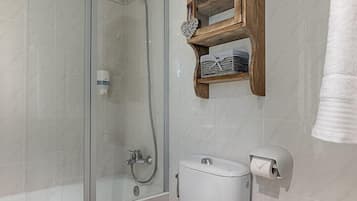 Un baño moderno con ducha envuelta en vidrio, inodoro, bidé y repisa de madera sobre el inodoro.