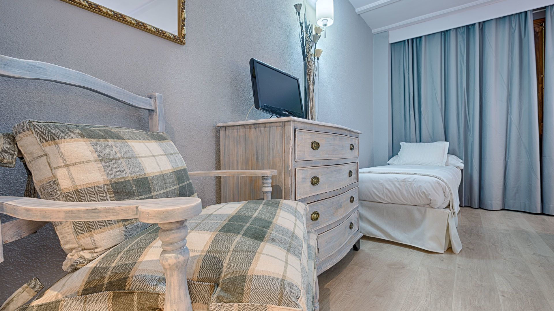 Una habitación de hotel con una cama, un aparador de madera, un televisor y una ventana con cortinas.