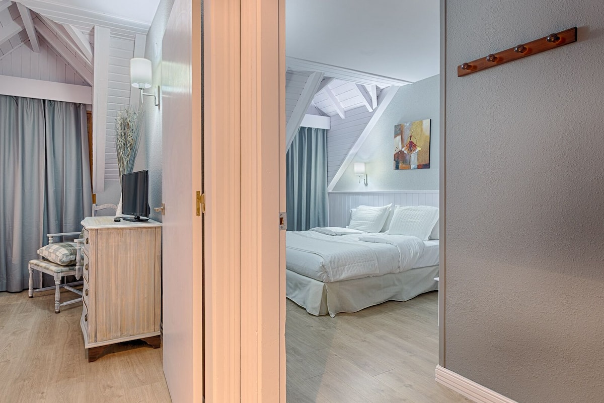 A bedroom with a bed, a bedside table, a chair, and a window with curtains.