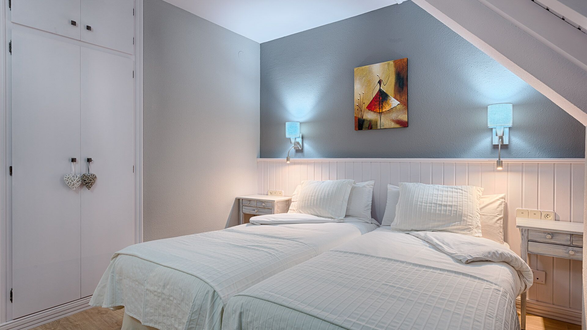 Ein Schlafzimmer mit schrägem Dach, einem Bett mit weißer Bettwäsche, zwei Nachttischen und einem Bild an der Wand.