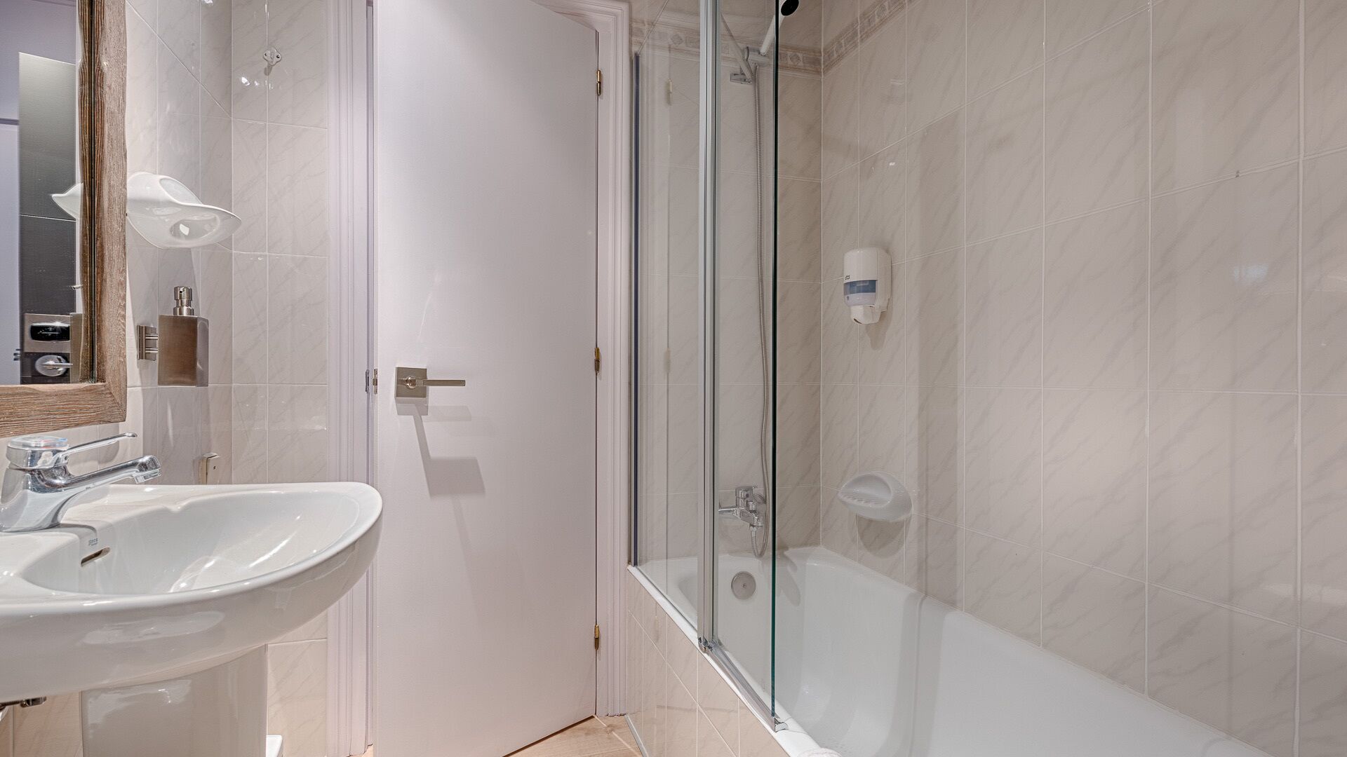 Un baño moderno con ducha envuelta en vidrio, un lavabo blanco y un espejo.
