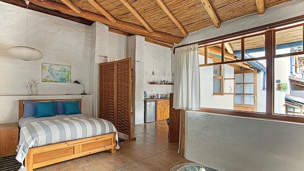A bedroom with a wooden bed, a small table, and a window with curtains. - Studio Mariposa with a fantastic garden in the historical Quito (Quito)