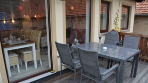 An outdoor dining area with a glass partition, a table with chairs, and a view of the interior through the glass.