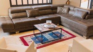 Ein Wohnzimmer mit einem braunen Ledersofa, einem Couchtisch mit Zeitschriften und einem Teppich mit blau-rotem Muster.