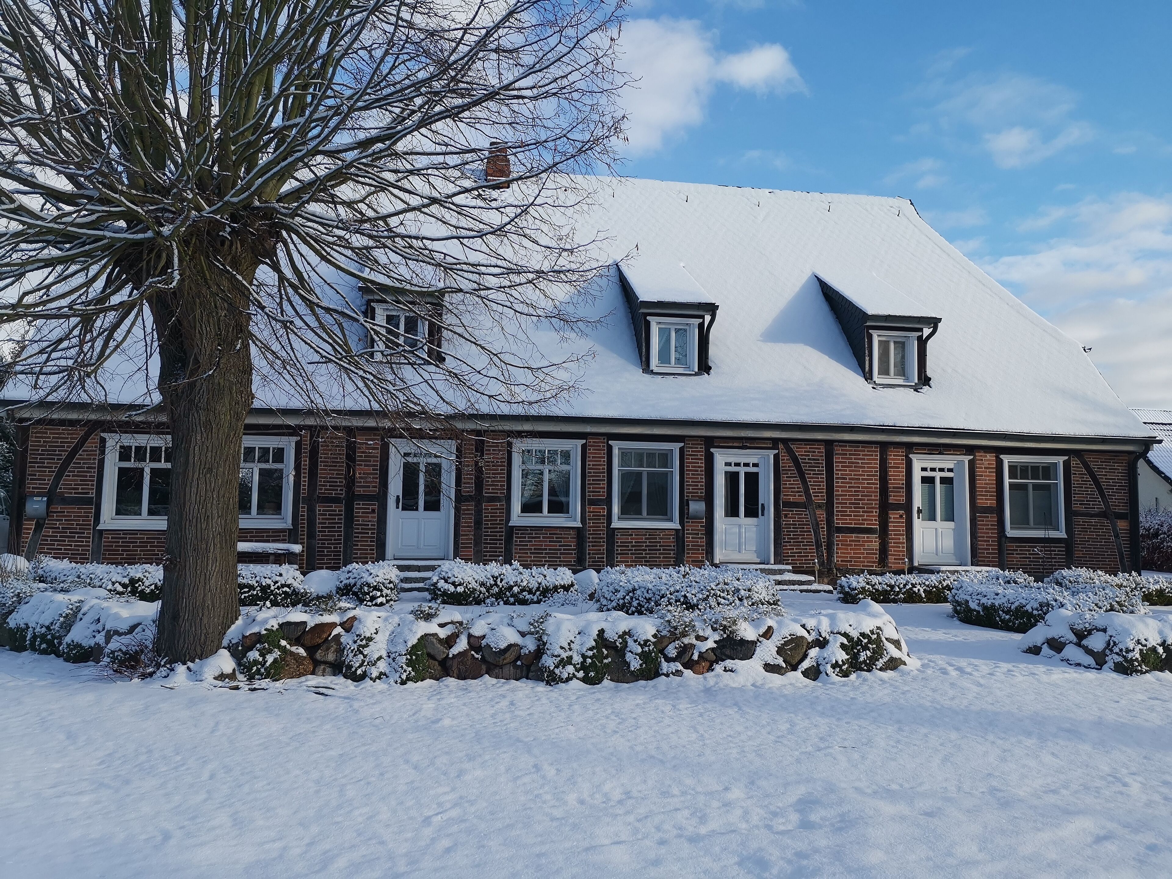 A two-story brick house with a snow-covered roof and a large tree in the foreground.