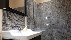 A bathroom with a white sink, a mirror, a shower with a glass door, and a tiled wall. - 58m² classic apartment for 2-4 people in the center (Wien)