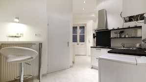 A modern kitchen with white cabinetry, a bar stool, a built-in oven, and a window with decorative curtains. - 58m² classic apartment for 2-4 people in the center (Wien)