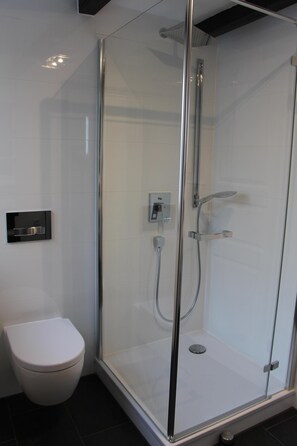 Un baño moderno con ducha de vidrio, inodoro blanco y panel de control en la pared.