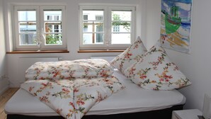 Un dormitorio con cama, dos ventanas, un radiador y un cuadro en la pared.