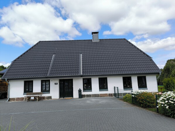 A white building with a dark roof, a number '20' sign, and a bench in front.