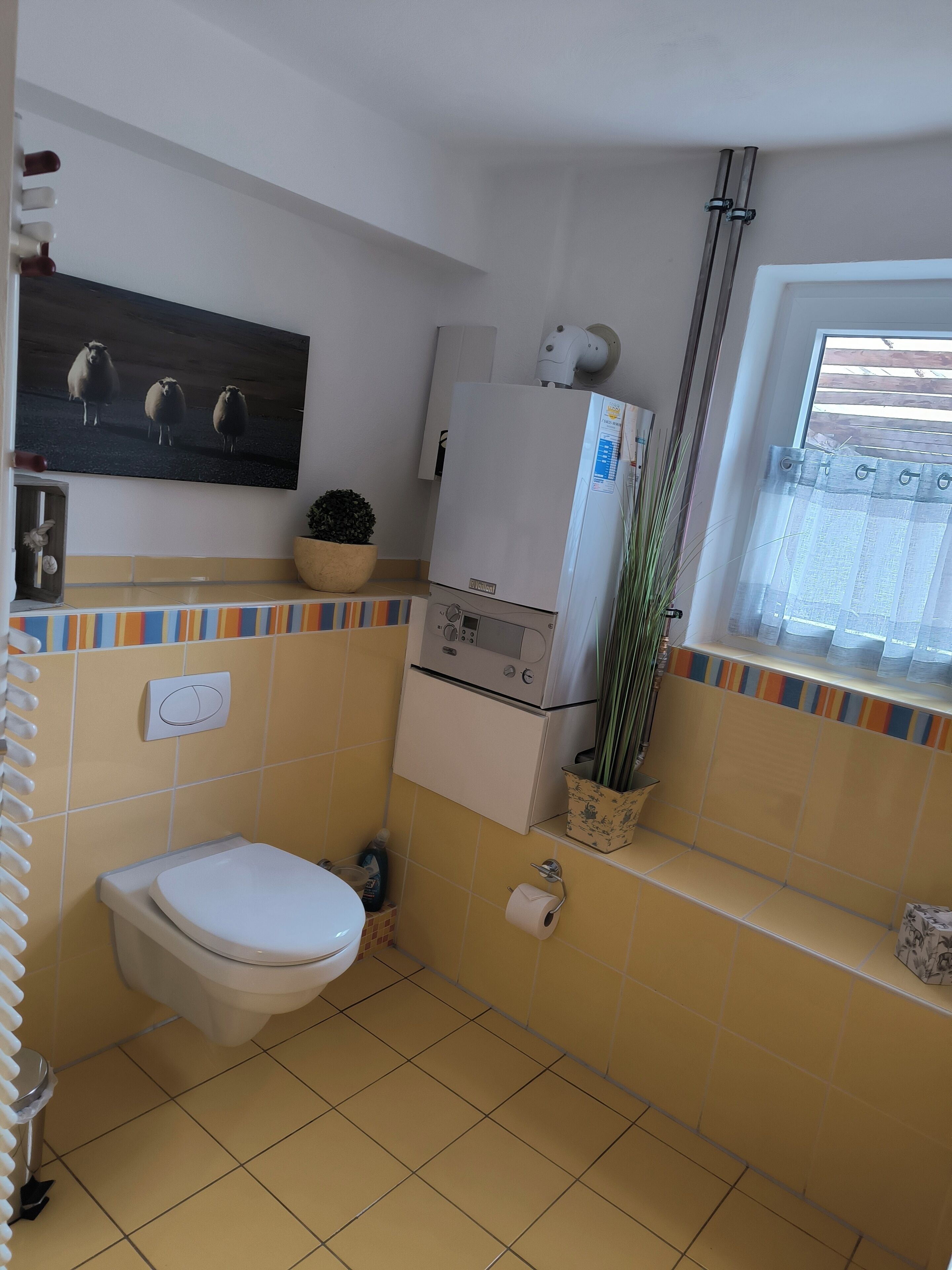 A bathroom with a toilet, a sink, a mirror, a heater, and a window with a curtain.