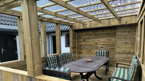 A wooden deck with a table and chairs, a bench, and a glass ceiling.
