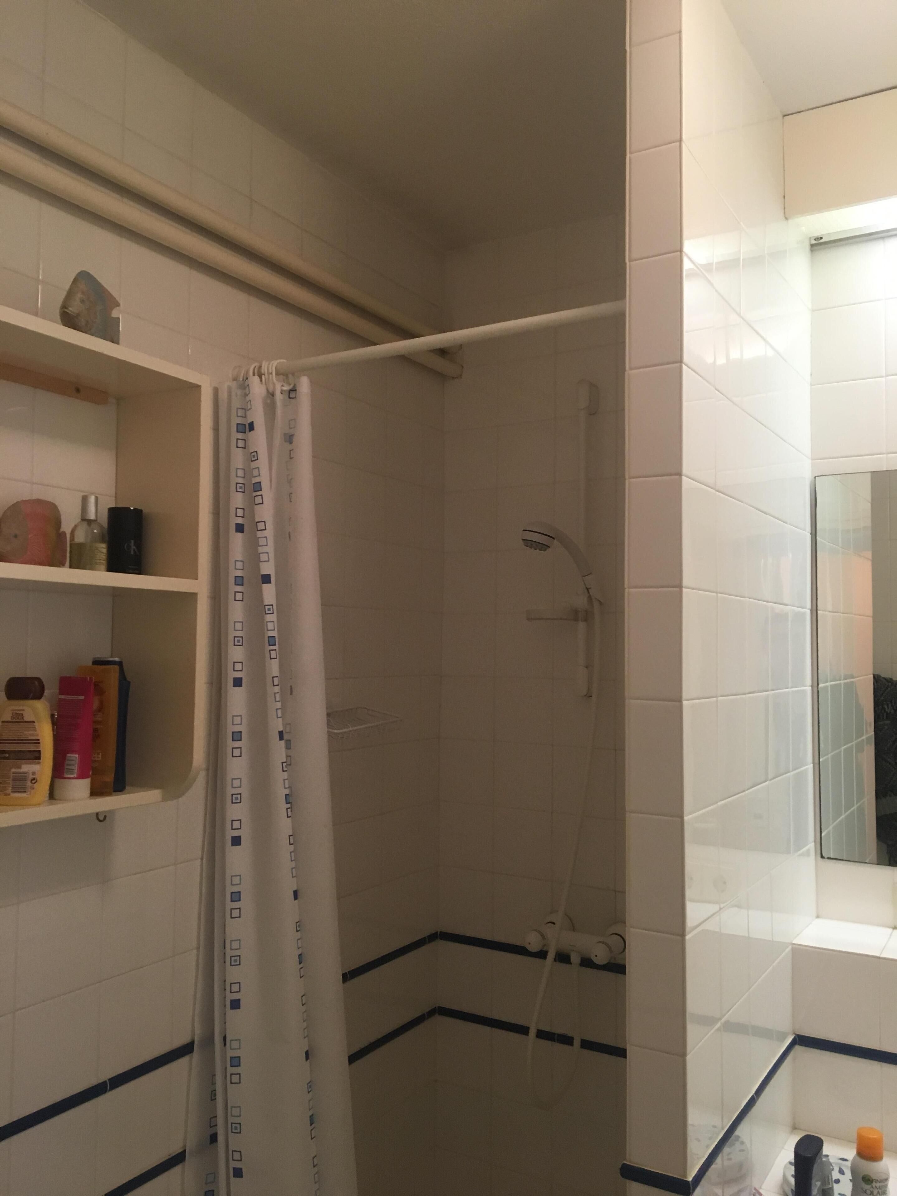 Une salle de bain avec une douche, des murs carrelés, une étagère avec des articles de toilette et un miroir.