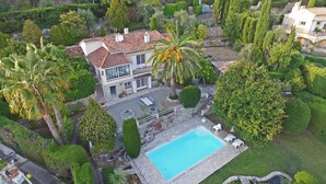 A large house with a swimming pool, surrounded by lush greenery and palm trees. - Private Family Villa with Heated Pool near Cannes (Spéracèdes)