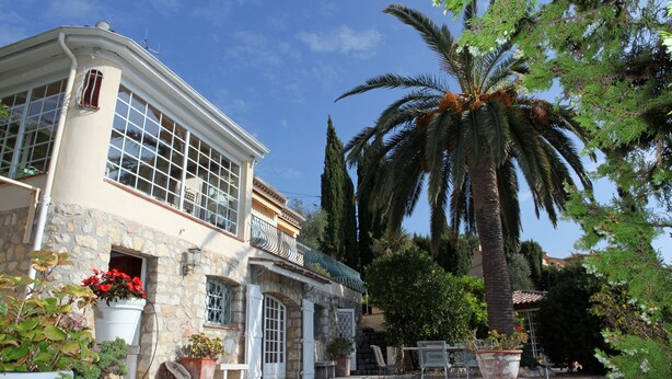 A stone building with large windows and a balcony, surrounded by potted plants and a palm tree. - Private Family Villa with Heated Pool near Cannes (Spéracèdes)