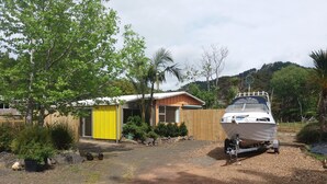 A house with a yellow shed, a boat on a trailer, and a dirt driveway.