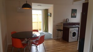 A compact kitchen with a washing machine, a dining area with a table and chairs, and a view of the outside through a door.