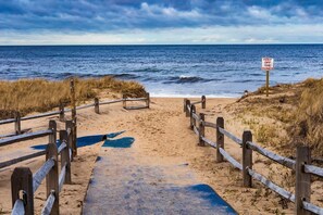 Un sentiero sulla spiaggia che conduce all'oceano, con un cartello che avvisa di non calpestare le dune.