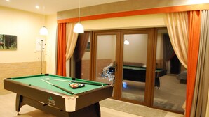 A pool table with balls, a lamp, and a view through a glass door into a room with a pool table. - Vacation home Jūrmalas Priedes (Apšuciems)