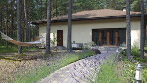 A modern house with a paved pathway, surrounded by tall trees and lavender plants. - Vacation home Jūrmalas Priedes (Apšuciems)