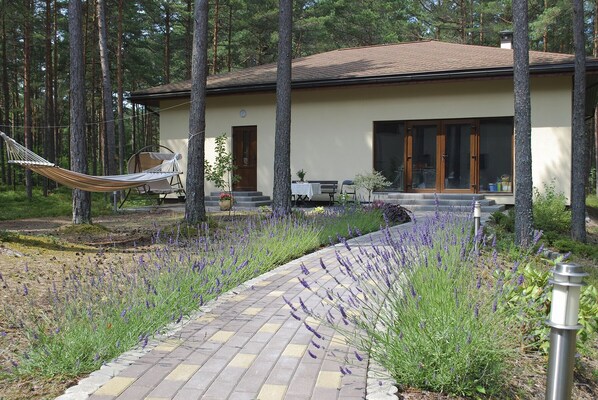 Una casa moderna con un camino empedrado, rodeada de árboles altos y plantas de lavanda.