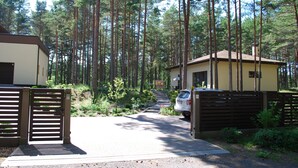 A forested area with a gated driveway leading to a building with a brown roof. - Vacation home Jūrmalas Priedes (Apšuciems)
