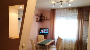 A dining area with a table and chairs, a television on a stand, and a window with curtains. - Exquisite apartment  (Sector 5)
