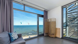 Ein modernes Zimmer mit großem Fenster zum Meer, einer Couch mit dekorativem Kissen und einem Korbschirm.